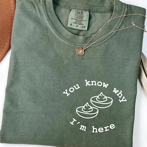 Può includere: Maglietta verde con testo bianco che recita "You know why I'm here" e una grafica di due metà di avocado con una cucchiaiata di guacamole in cima.