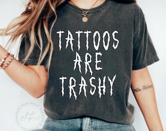 May include: A dark gray t-shirt with the text "Tattoos Are Trashy" printed in white with a jagged font.