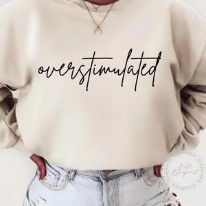 May include: A cream-colored sweatshirt with the text "overstimulated" written in black cursive script.