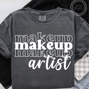 May include: Dark gray crew neck sweatshirt with the words "makeup makeup makeup artist" in white, stacked vertically. The sweatshirt has a vintage, washed look. A phone with a checkered case is visible.