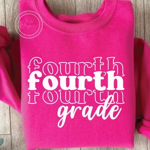 May include: A bright pink sweatshirt with the words "Fourth Grade" in white, stacked vertically. The sweatshirt has a crew neck and long sleeves. The text is in a bold, playful font.