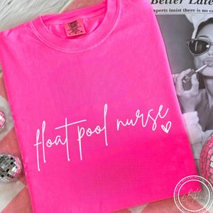 May include: Vibrant pink crew neck t-shirt with the words "float pool nurse" in white script. A small white heart follows "nurse". The shirt is made of a soft material.