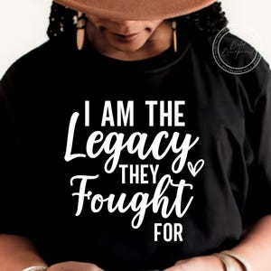 Pode incluir: T-shirt preto com o texto branco "I AM THE Legacy THEY FOUGHT FOR". O texto está em uma fonte elegante e cursiva. A camisa é um estilo clássico de gola redonda.