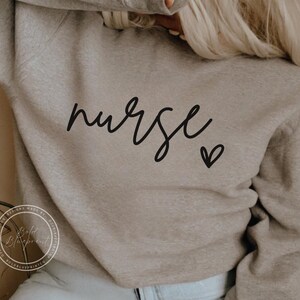 Peut inclure: Un sweat-shirt gris avec le mot "nurse" &eacute;crit en cursive noire et un petit c&oelig;ur noir.