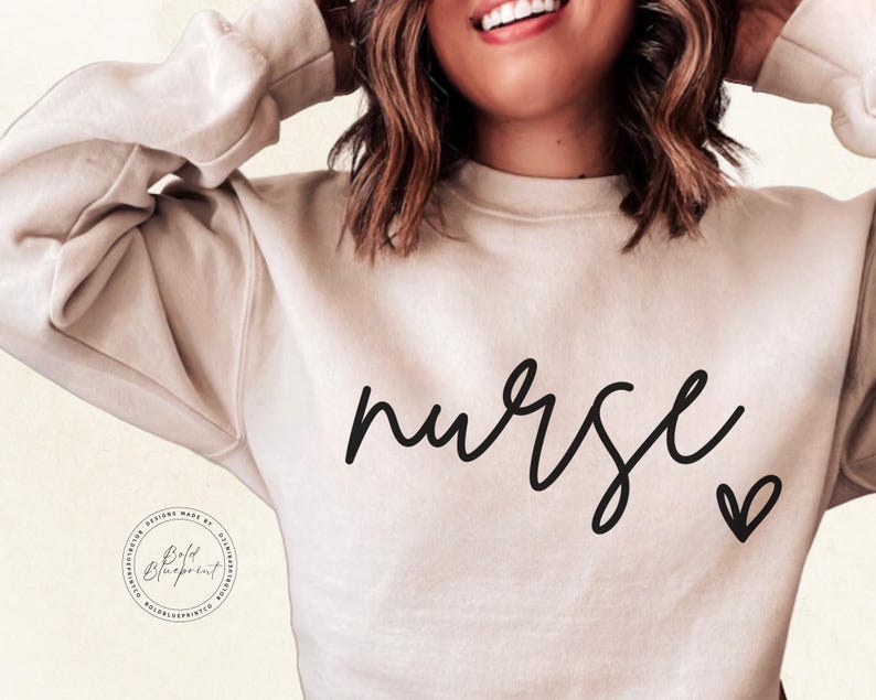 Peut inclure: Un sweat-shirt beige clair avec le mot "nurse" &eacute;crit en cursive noire et un petit c&oelig;ur noir &agrave; droite du mot.