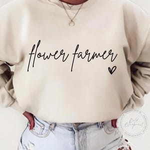 May include: A cream colored sweatshirt with the text "flower farmer" in black script with a small heart symbol.