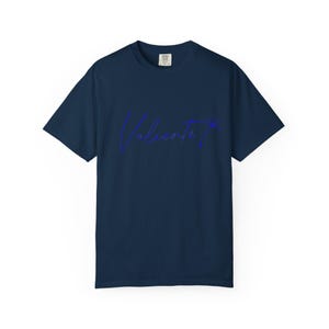 Op de afbeelding: Marineblauw T-shirt met het woord "Valiente" in een blauw scriptlettertype. Het woord is licht gebogen en heeft een klein stervormig ontwerp aan het einde. Het shirt is effen van kleur en heeft korte mouwen.