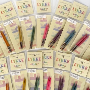 May include: A collection of LYKKE Colour wooden knitting needles in various sizes and colors. Each pair is packaged with a label displaying the size in US and metric measurements. The needles are in shades of red, orange, green, purple, and blue.