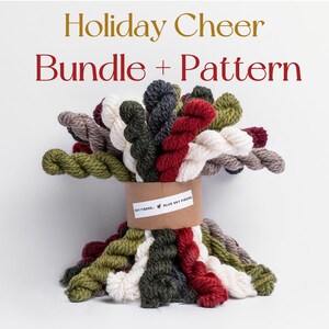 May include: A bundle of colorful yarn skeins in shades of green, red, white, gray, and brown, tied together with a brown paper band. The text "Holiday Cheer Bundle + Pattern" is displayed above the yarn.