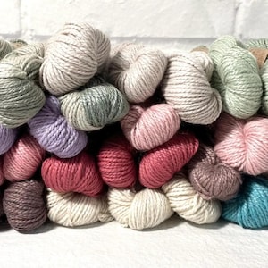 May include: A collection of yarn skeins in various colors, including beige, pink, green, purple, and blue. The yarn is arranged in a pile, with some skeins overlapping.