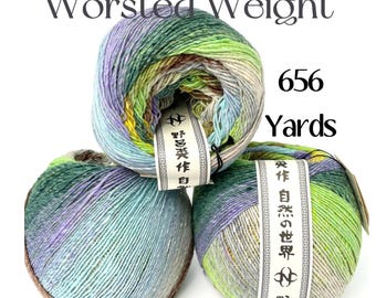 May include: Three balls of worsted weight yarn featuring a variegated color palette of green, blue, purple, and brown. Each ball has a white paper label with black Japanese text and a logo. The text "Worsted Weight" and "656 Yards" is visible.