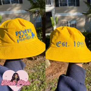 Könnte beinhalten: Zwei gelbe Bucket-Hats mit blauem Text. Der erste Hut sagt "Pretty Sigma Poodle" mit einer Poodlesilhouette. Der zweite Hut sagt "Est. 19" mit einem Handsymbol.