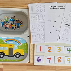 May include: A set of educational materials for learning numbers. The set includes a tray with small figures, a sheet with numbers and stars, a sheet with numbers to trace, and a set of number cards from 1 to 10.