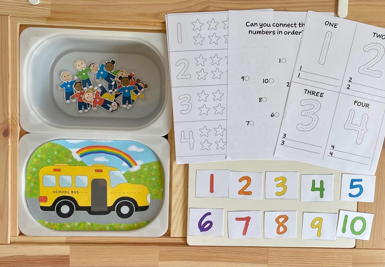 May include: A set of educational materials for learning numbers. The set includes a tray with small figures, a sheet with numbers and stars, a sheet with numbers to trace, and a set of number cards from 1 to 10.