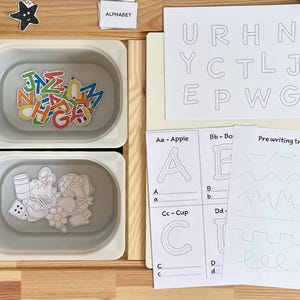 May include: A set of alphabet learning materials for children. The set includes a tray with magnetic letters, a sheet with uppercase letters to trace, and a sheet with lowercase letters to trace. The set also includes a sheet with pre-writing tracing exercises.