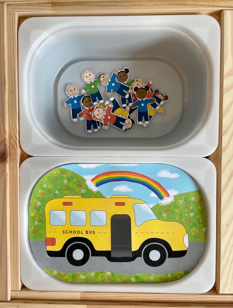 May include: A white oval container with a yellow school bus with a rainbow above it. The bus has the words "SCHOOL BUS" on the side. There are also small paper dolls inside the container.