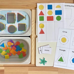 May include: A set of colorful foam shapes in a white container, along with a worksheet with various shapes and the text "How many shapes fit inside?"  The worksheet also includes the words "Circle", "Square", "Triangle", and "Hexagon".