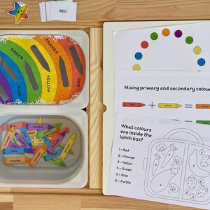 May include: A rainbow-colored activity set for learning about colors. The set includes a rainbow with slots for crayons, a container of crayons, and a worksheet with a lunchbox to color in. The worksheet also includes instructions for mixing primary and secondary colors.