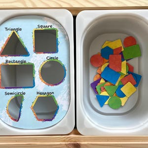 May include: A white tray with cutouts of different shapes: triangle, square, rectangle, circle, semicircle, and hexagon. A separate white tray contains a variety of colorful shapes, including circles, squares, triangles, and rectangles.