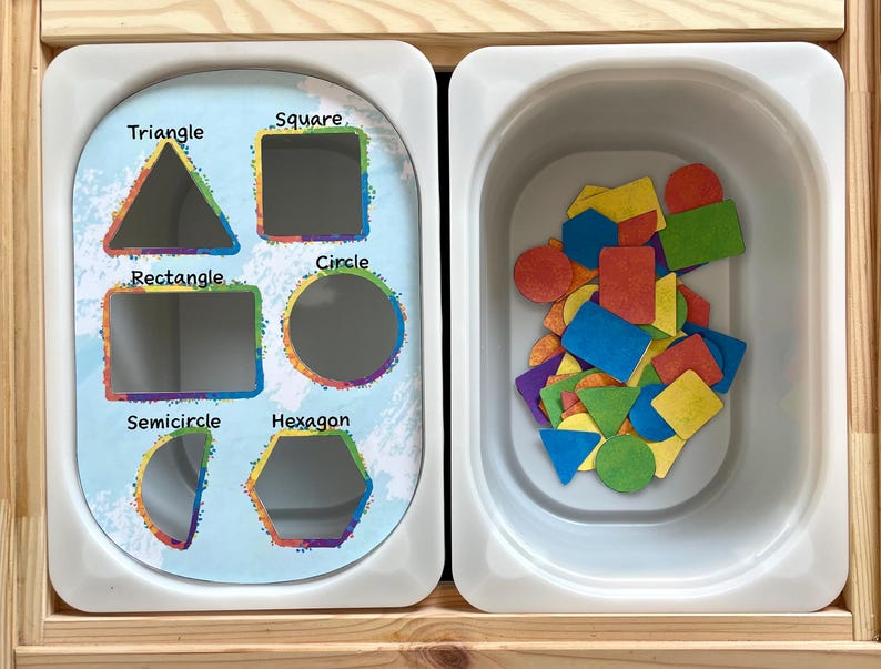 May include: A white tray with cutouts of different shapes: triangle, square, rectangle, circle, semicircle, and hexagon. A separate white tray contains a variety of colorful shapes, including circles, squares, triangles, and rectangles.