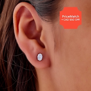 May include: A close-up of an ear with a single oval-shaped stud earring. The earring is set in a silver metal and features a clear, sparkling stone. The skin tone is light.