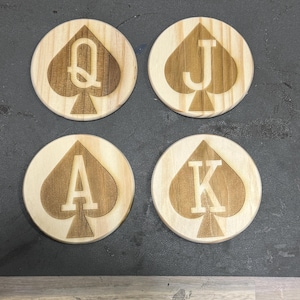 May include: Four wooden coasters with a spade design and the letters A, K, Q, and J in white.