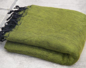 Pode incluir: Uma manta verde-oliva dobrada com uma trama texturizada e franjas pretas em uma das bordas. O tecido apresenta uma aparência sutilmente mesclada com variações no tom de verde por toda a superfície do material, criando um efeito visual único.