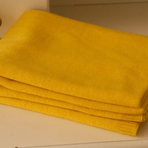May include: A folded, bright yellow blanket. The blanket is neatly stacked, showcasing its soft texture. The colour is a vibrant, sunny yellow, creating a warm and inviting aesthetic. The folded edges and layers are clearly visible.