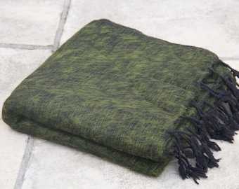 Pode incluir: Uma manta retangular dobrada com um padrão texturizado mosqueado em verde-oliva e preto. A manta é finalizada com longas franjas pretas ao longo de uma borda, criando um contraste distinto com o tecido verde profundo da peça inteira.