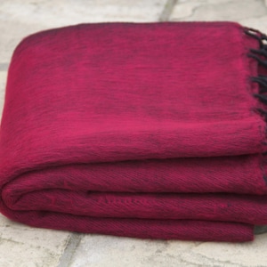 Op de afbeelding: Een gevouwen bordeauxrode wollen sjaal met zwarte franjes. De sjaal is gemaakt van zachte, warme wol en is perfect om je warm te houden op koude dagen.