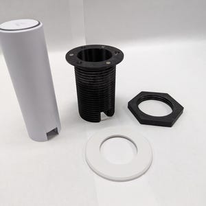 Puede incluir: Un conjunto de cuatro piezas de plástico blanco y negro para una lámpara o un accesorio de iluminación. Las piezas incluyen una base cilíndrica, un anillo roscado, un anillo plano y una tuerca hexagonal.