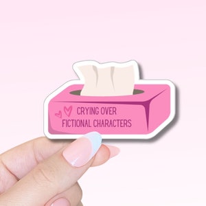Puede incluir: Pegatina rosa de caja de pañuelos con el texto "Crying over fictional characters" y dos corazones rosas.