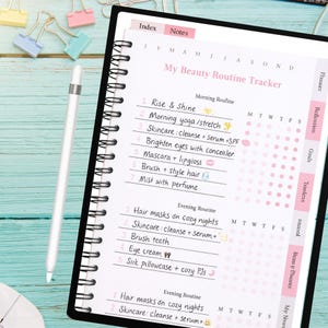 May include: A black spiral-bound planner with a pink and white beauty routine tracker. The planner includes sections for morning and evening routines, with prompts for skincare, hair care, and other beauty tasks. A white stylus pen rests on the planner.