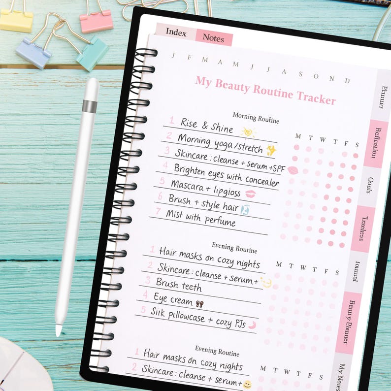 May include: A black spiral-bound planner with a pink and white beauty routine tracker. The planner includes sections for morning and evening routines, with prompts for skincare, hair care, and other beauty tasks. A white stylus pen rests on the planner.