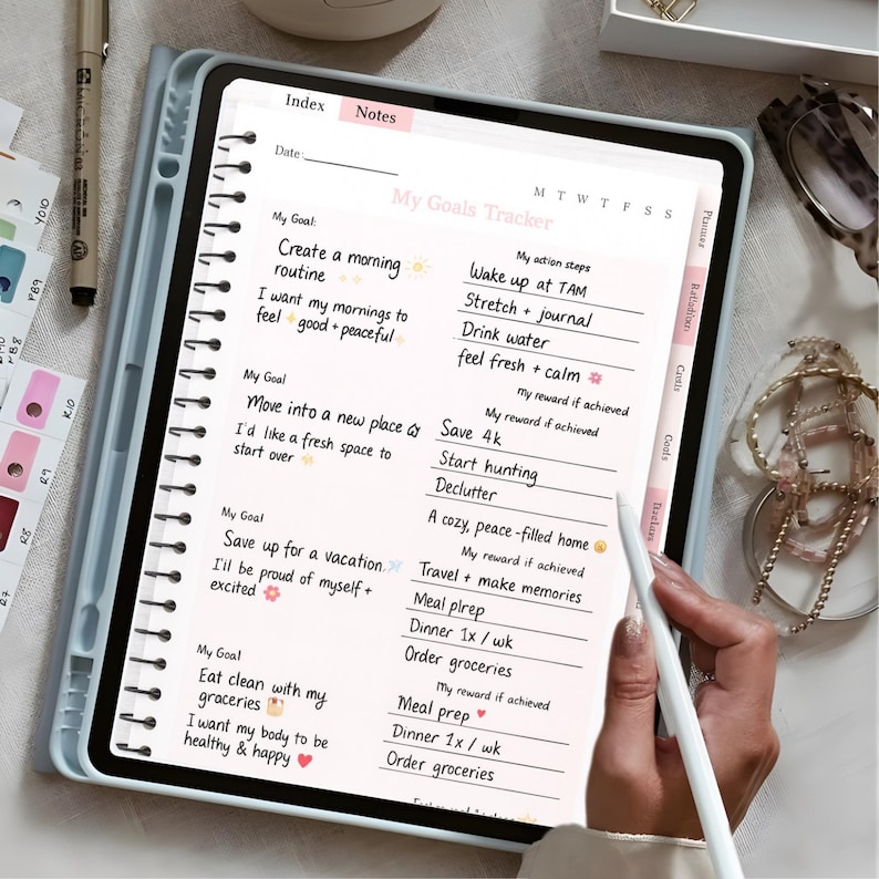 May include: A digital planner in a light blue case, displaying a "My Goals Tracker" page. The page features handwritten goals and action steps, such as "Wake up at TAM" and "Declutter." A stylus is positioned near the screen.