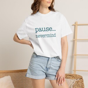 May include: A white short-sleeved t-shirt featuring the dark teal text "pause... nevermind" printed in a simple, clean font across the chest. The garment has a classic crew neckline and a standard fit, providing a neutral and versatile appearance.