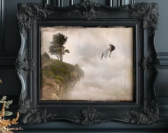 May include: A black ornate frame with a vintage-style print of a woman falling from a cliff into a foggy landscape. The woman is wearing a white dress and has long dark hair. The print is set against a dark gray background.
