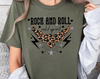 May include: A green t-shirt with a graphic of a leopard print eagle with lightning bolts and stars. The text "Rock and Roll" and "wild spirit" is printed on the shirt.