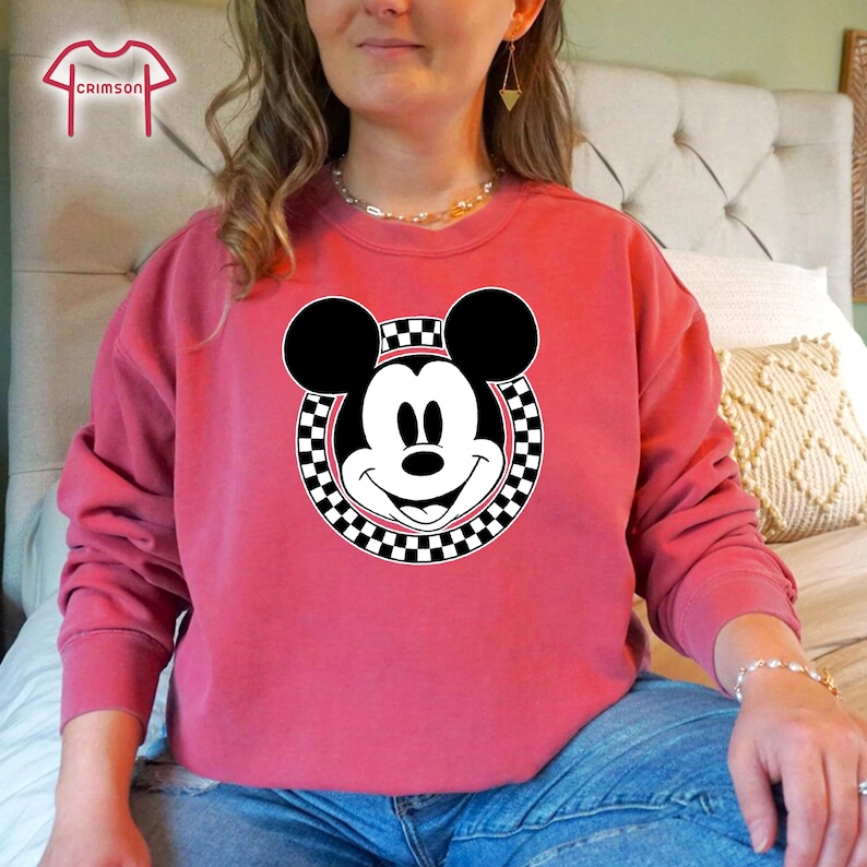 Peut inclure: Un sweat-shirt rose avec un cercle &agrave; carreaux noirs et blancs autour d'une image de dessin anim&eacute; de Mickey Mouse.