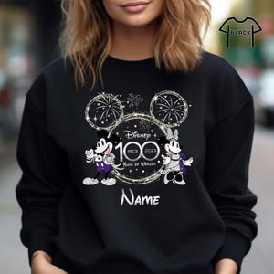 May include: Black sweatshirt with a silver glitter design featuring Mickey and Minnie Mouse. The design includes fireworks, Mickey Mouse ears, and the text "Disney 100 1923 2023 100 Years of Wonder".