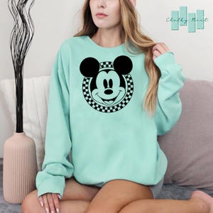 Peut inclure: Un sweat-shirt vert clair avec un cercle &agrave; carreaux noir et blanc autour d'une image noir et blanc du visage de Mickey Mouse.