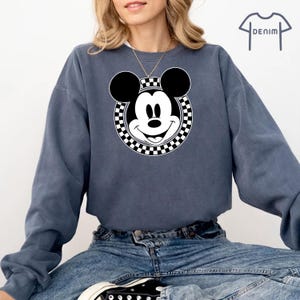 Peut inclure: Un sweat-shirt bleu avec un cercle &agrave; carreaux blancs et noirs repr&eacute;sentant le visage de Mickey Mouse. Le sweat-shirt a des manches longues et un col rond.
