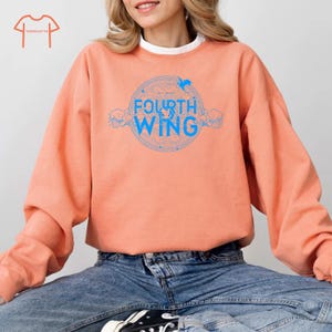 May include: A peach-colored sweatshirt with a blue graphic design that says "FOURTH WING" in a circle with a bird design above the text.