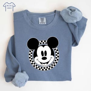 Peut inclure: Un sweat-shirt bleu avec un cercle &agrave; carreaux noirs et blancs autour d'un visage de Mickey Mouse blanc.