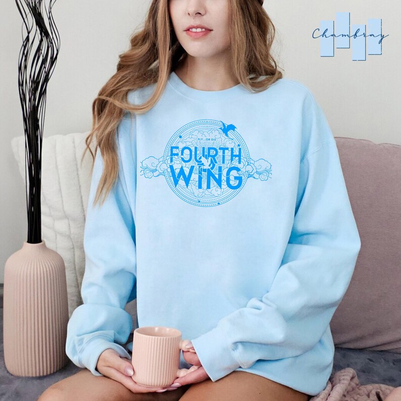 May include: A light blue sweatshirt with a graphic design of a circle with the words "The Law of" and "Fourth Wing" inside. The graphic also includes a bird and clouds.