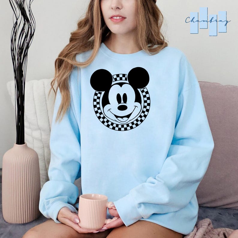Peut inclure: Un sweat-shirt bleu clair avec un motif circulaire noir et blanc &agrave; carreaux repr&eacute;sentant le visage de Mickey Mouse.