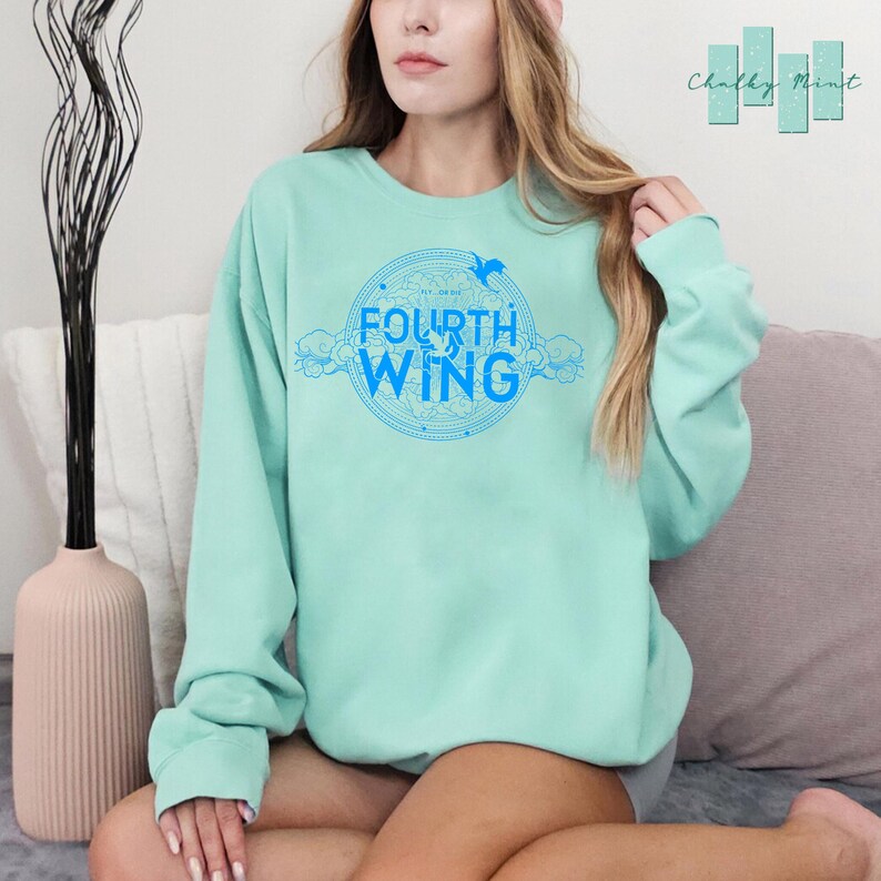 May include: A light blue sweatshirt with a blue graphic design of a circle with the words "The Fourth Wing" and a bird inside the circle.