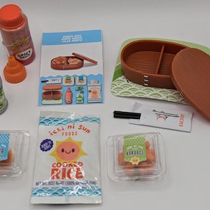 Peut inclure: Un ensemble d'aliments miniatures pour une maison de poupée ou une cuisine de jeu. L'ensemble comprend une boîte bento en bois brun, deux petits contenants en plastique de nourriture, un paquet de riz cuit et deux petites bouteilles de sauce. Les contenants de nourriture sont étiquetés "Gyoza" et "Kakaraage".