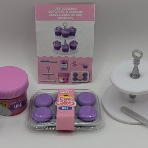 Peut inclure: Un ensemble de fournitures de pâtisserie pour cupcakes Ube, de couleur violette et blanche. L'ensemble comprend un présentoir à gâteaux à deux étages, un petit récipient de pépites violettes, un récipient de glaçage violet et un plateau de six cupcakes violets. L'emballage comprend le texte "UBE SWEETS CUP CAKES UBE".