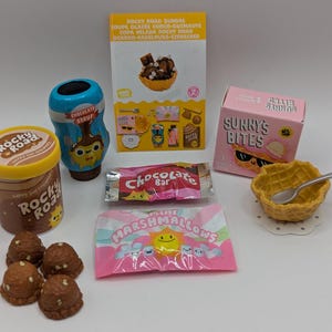 Peut inclure: Une collection d'articles miniatures sur le thème du sundae à la crème glacée, comprenant une barre de chocolat, un sac de guimauves, un petit bol de crème glacée, une bouteille de sirop de chocolat et un récipient de crème glacée au chocolat et aux noix. Les articles sont tous de couleurs vives et ont un design amusant et fantaisiste.